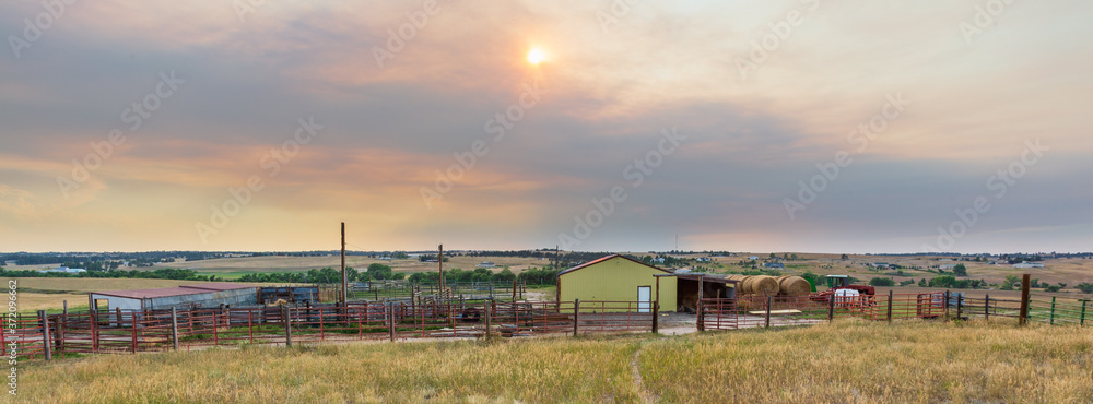 Pastoral scene at sunset on a working ranch near Denver with barn, large round hay bales, sheds, corrals, metal and wood fencing
