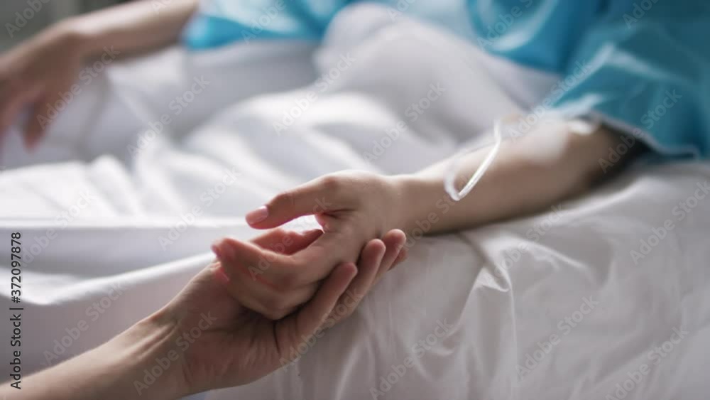 Handheld close up shot of unrecognizable man caressing hand of weak woman receiving treatment in hospital Handheld close up shot of unrecognizable man caressing hand of weak woman receiving treatment in hospital