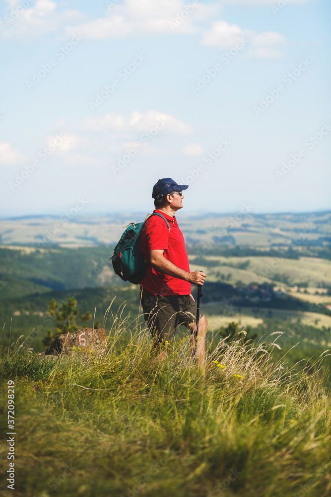 Naklejka premium Active man with backpack hiking in mountain forest in the summer, selective focus