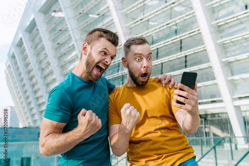 Fototapete Men celebrating money win in online sport gambling application with football sta