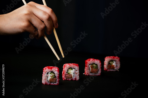 Female hand takes chopsticks california sushi rolls with Chinese chopsticks. Selective focus, black background