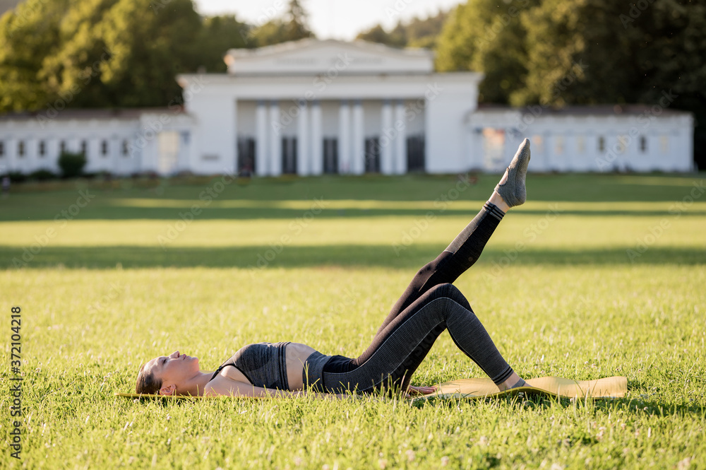 Fototapeta premium Beautiful young woman lying on a yellow mattress doing pilates or yoga, one leg stretch beginner exercises