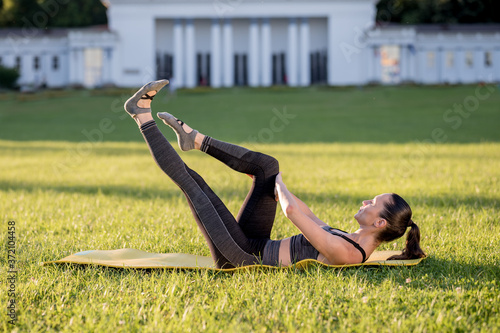 Beautiful young woman lying on a yellow mattress doing pilates or yoga, single leg stretch intermediate exercises