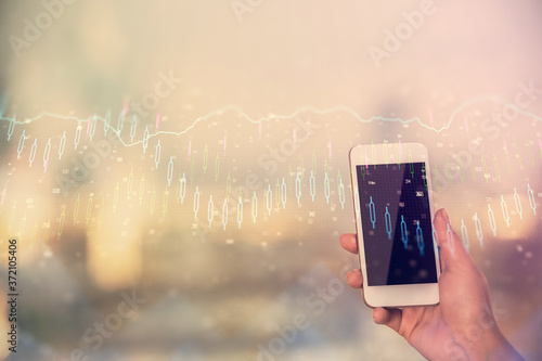 Double exposure of forex chart sketch hologram and woman holding and using a mobile device. Stock market concept.