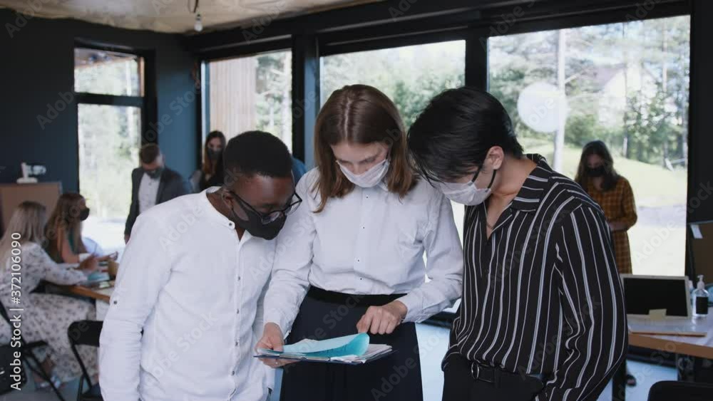 Young happy diverse gen-z business colleagues work together, all wearing COVID-19 face masks at modern light office. Young happy diverse gen-z business colleagues work together, all wearing COVID-19 face masks at modern light office.