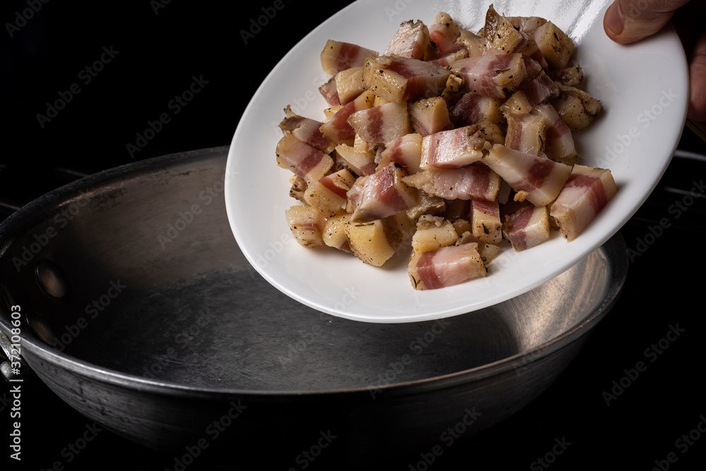 Preparing Spaghetti Carbonara on a black stove with pork guanciale on a white plate on an aluminum pan Preparing Spaghetti Carbonara on a black stove with pork guanciale on a white plate on an aluminum pan