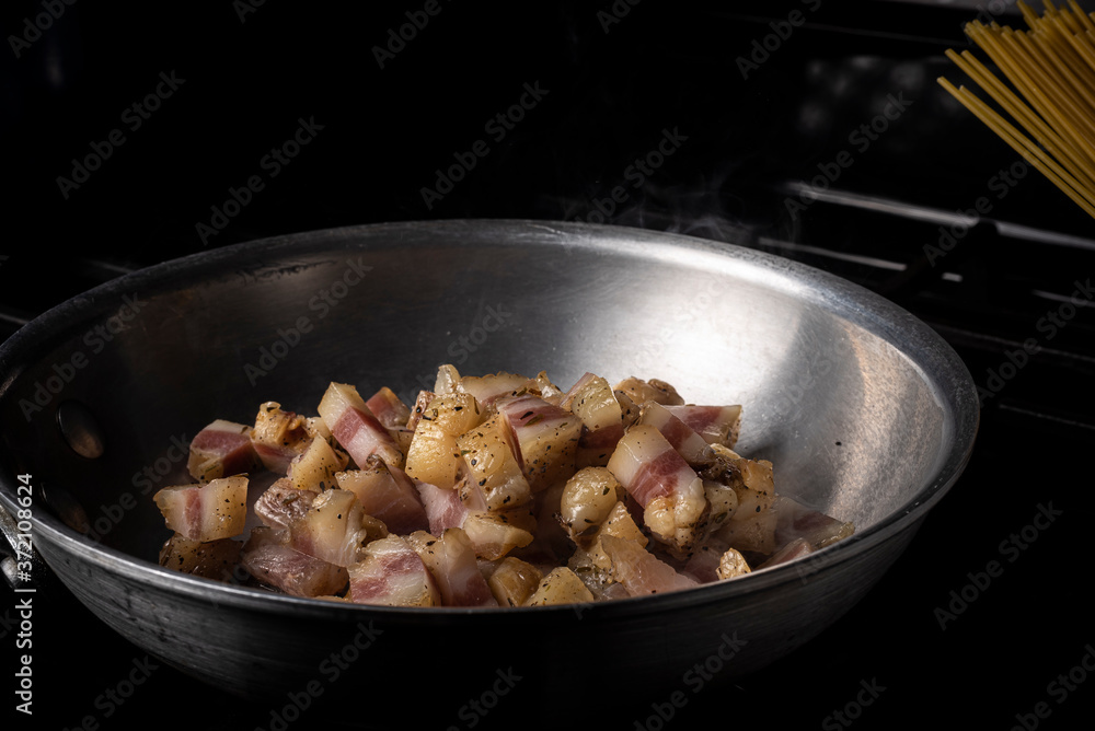 Preparing Spaghetti Carbonara on a black stove with pork guanciale in an aluminum pan Preparing Spaghetti Carbonara on a black stove with pork guanciale in an aluminum pan