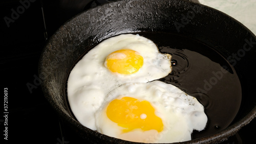 chicken eggs, fried eggs in a cast iron pan close-up, breakfast, omelet, two eggs with yellow yolks are fried on the stove