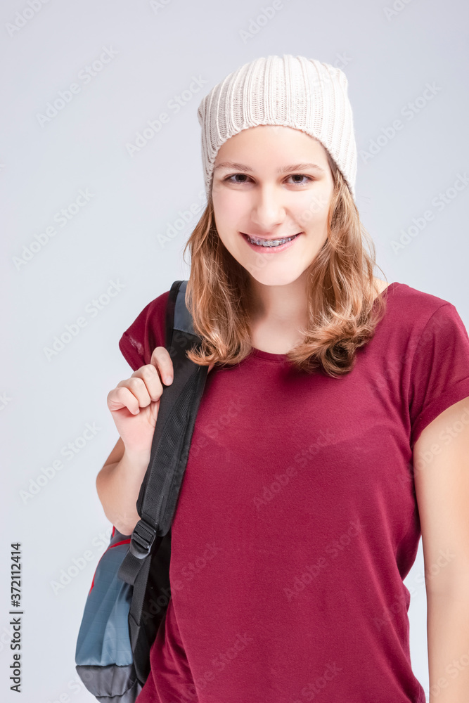 Teenage Medical Ideas. Portrait Of Caucasian Teenager Girl Wearing Teeth Brackets. Posing with Backpack Indoors. Teenage Medical Ideas. Portrait Of Caucasian Teenager Girl Wearing Teeth Brackets. Posing with Backpack Indoors.