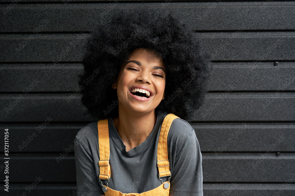 Happy stylish African American teen girl wearing yellow trendy sundress  with Afro hair looking at camera laughing on black background. Smiling  mixed race hipster woman headshot closeup portrait. Stock Photo | Adobe