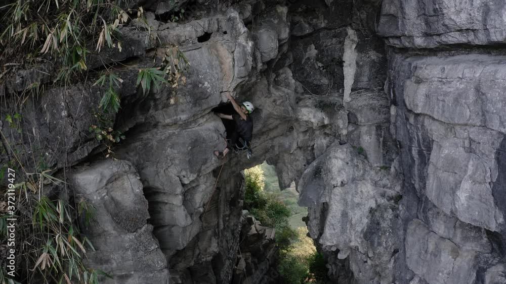 Rock climber ascending Treasure Cave in Yangshuo China, stone mountainside, aerial Rock climber ascending Treasure Cave in Yangshuo China, stone mountainside, aerial
