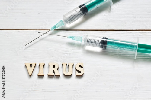Syringes for injection on a white wooden background. Virus inscription in wooden letters. Vaccine against the virus. Medicine concept. photo