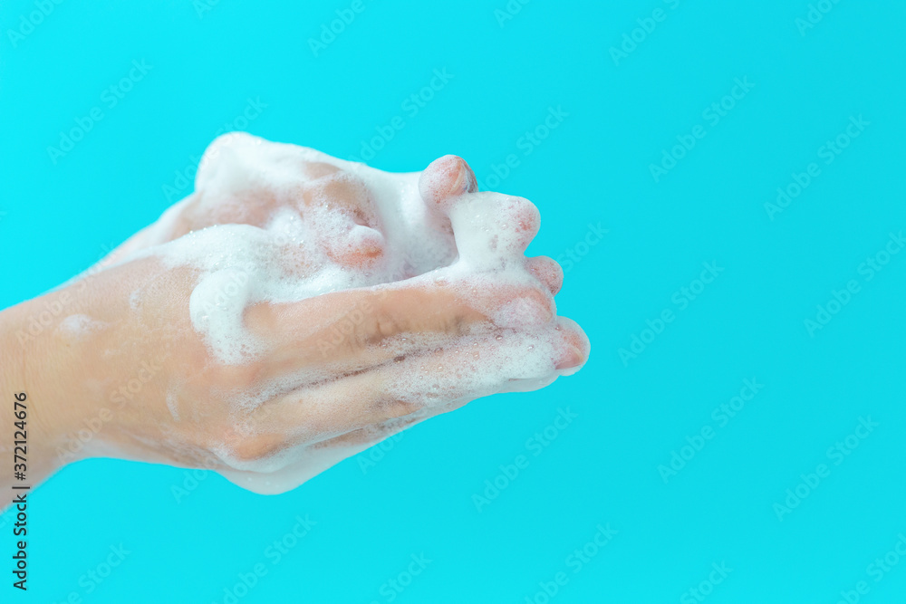 Fototapeta premium The girl washes her hands with foam on blue background, side view
