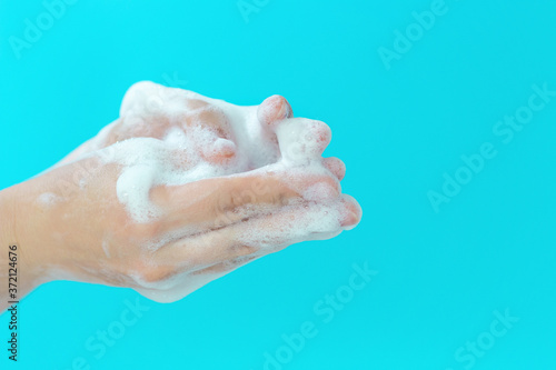 The girl washes her hands with foam on blue background, side view