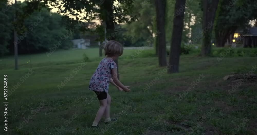 Behind and profile view of young cute innocent Caucasian girl in backyard walking and trying to catch lightning bugs at dusk, handheld pan slow motion Behind and profile view of young cute innocent Caucasian girl in backyard walking and trying to catch lightning bugs at dusk, handheld pan slow motion