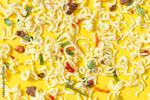 Dry noodles with spices broken down lies on yellow background