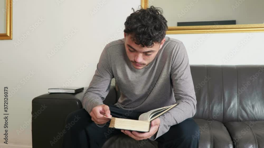 Mixed race guy sitting on couch reading the bible and praying Mixed race guy sitting on couch reading the bible and praying