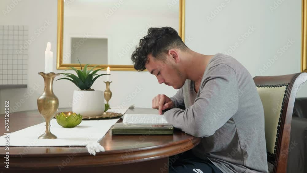 Mixed race guy reading the bible and turning page sitting by table. Mixed race guy reading the bible and turning page sitting by table.