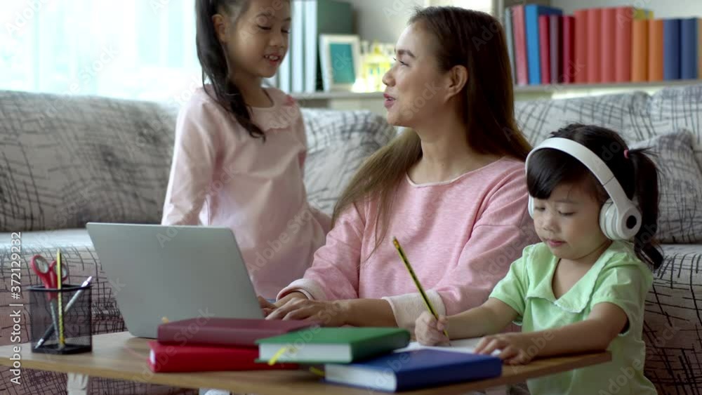 A Beautiful Asian mother busy working at home while looking after and teaching her children on a laptop computer A Beautiful Asian mother busy working at home while looking after and teaching her children on a laptop computer
