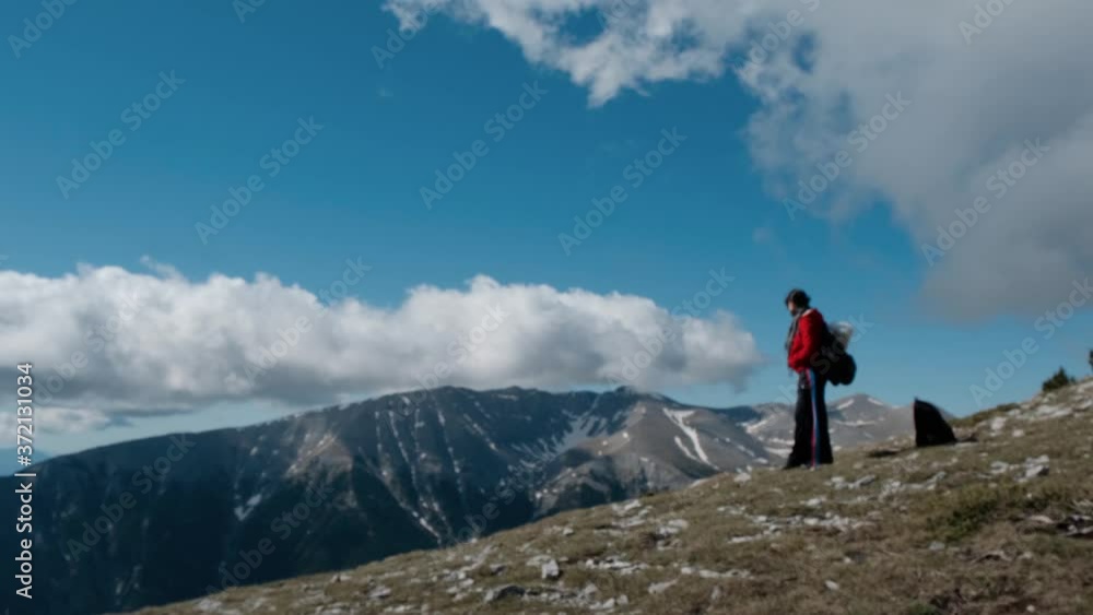 A Woman Hiker Standing On Top Of Mount Olympus In Greece Against A Cloudy Blue Sky - Wide Shot Pan Left A Woman Hiker Standing On Top Of Mount Olympus In Greece Against A Cloudy Blue Sky - Wide Shot Pan Left