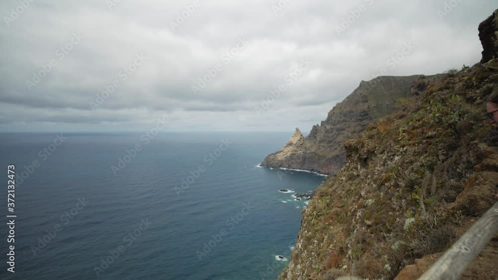 A female hiker enjoying the panoramic view over the ocean in Anaga mountains on Tenerife, Spain. Push in wide angle shot. A female hiker enjoying the panoramic view over the ocean in Anaga mountains on Tenerife, Spain. Push in wide angle shot.