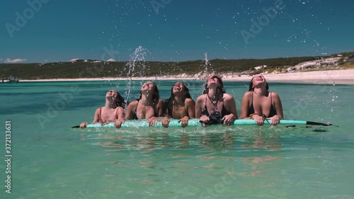 Pretty young girls lying on surfboard throwing hairs into air during beautiful sunny day at Hamelin Bay
