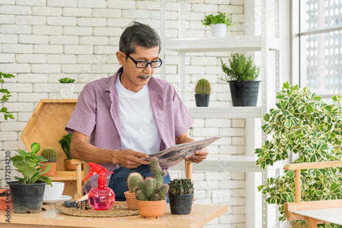 Senior asian retirement old man in casual outfit wearing glasses sitting and reading newspaper in modern green garden house