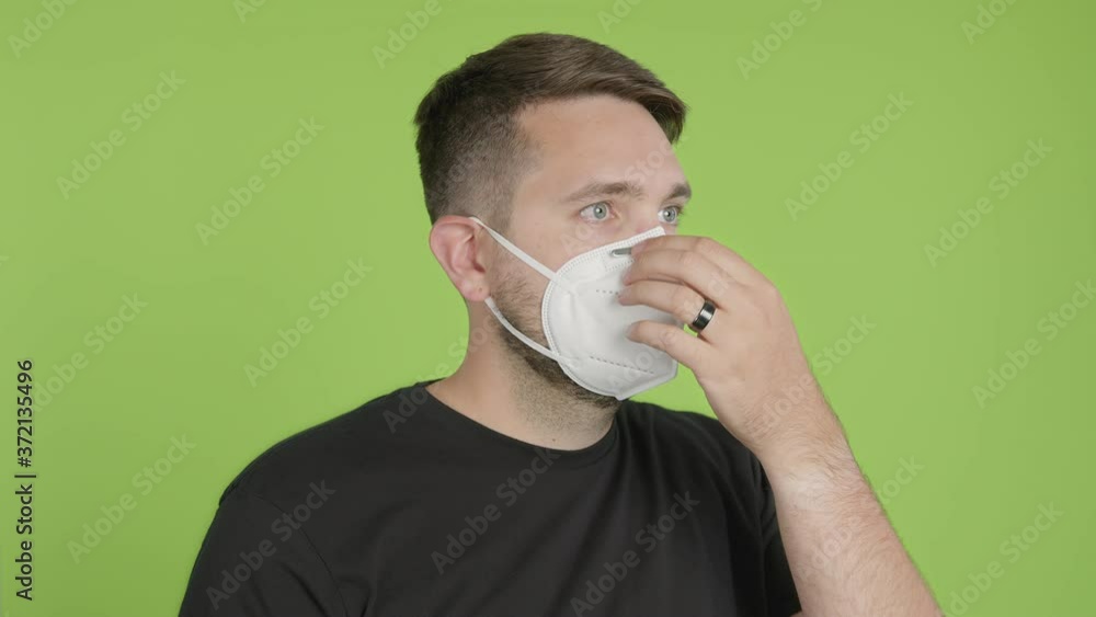 Man Puts on Protective KN95 Face Mask While Looking Right of Camera on Green Screen Chroma Key Man Puts on Protective KN95 Face Mask While Looking Right of Camera on Green Screen Chroma Key