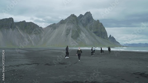 Group of People Walking on Black Sand Beach Under Vestahorn Mountain, Iceland.  Scenic Volcanic Landscape Sightseeing photo