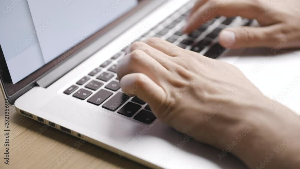 Close shot from diagonally above of male hands typing on laptop keys Close shot from diagonally above of male hands typing on laptop keys