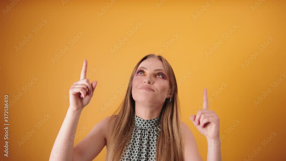 Happy woman with makeup looking and pointing above her. Yellow background Happy woman with makeup looking and pointing above her. Yellow background
