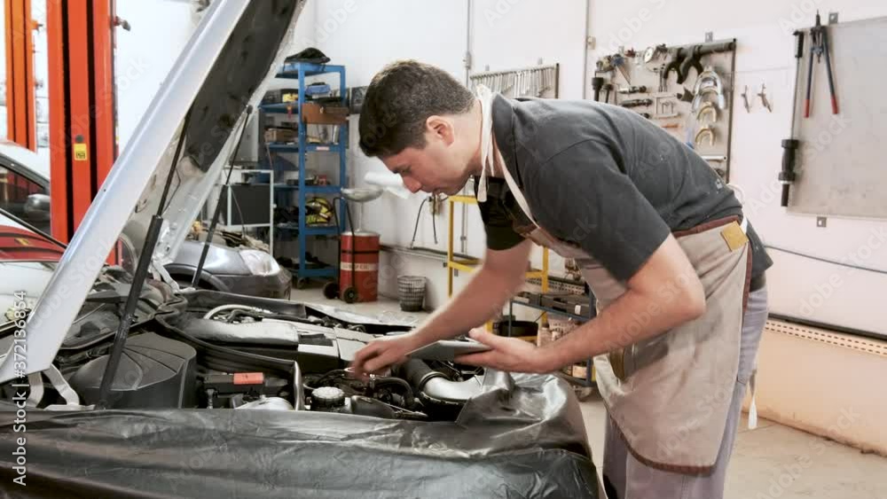 A professional mechanic inspects a car engine for faults or defects in a professional garage. A professional mechanic inspects a car engine for faults or defects in a professional garage.