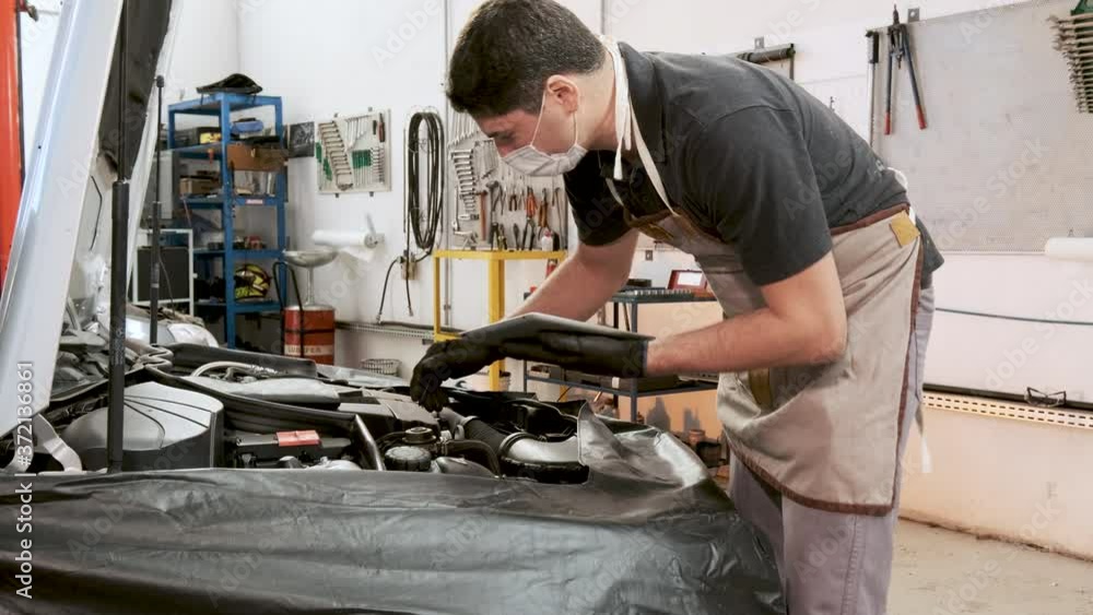 Skilled mechanic wearing protective face mask and gloves in his working environment. Handheld shot. Skilled mechanic wearing protective face mask and gloves in his working environment. Handheld shot.
