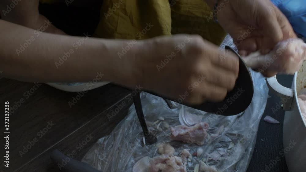 UK Asian Woman Using Traditional Vegetable Cutter To Cut Raw Chicken Leg. Locked Off UK Asian Woman Using Traditional Vegetable Cutter To Cut Raw Chicken Leg. Locked Off
