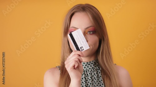 Happy glamour woman holding and looking credit card isolated on yellow photo