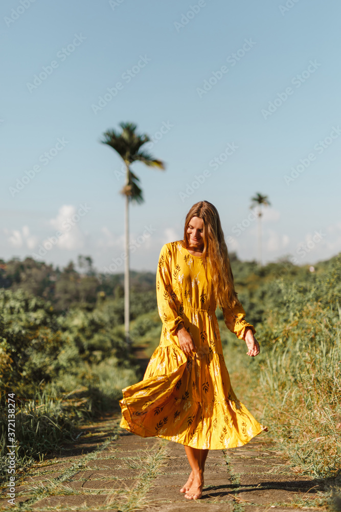 Young happy traveller woman in yellow dress walking on Campuhan Ridge way of artists, in Bali Young happy traveller woman in yellow dress walking on Campuhan Ridge way of artists, in Bali