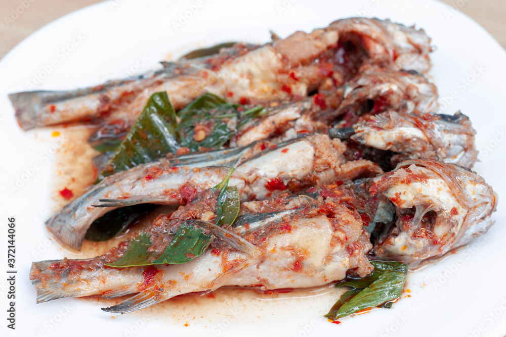 Fried twospot catfish in red spicy curry sauce or Chuchee in white plate on wooden table. Fried twospot catfish in red spicy curry sauce or Chuchee in white plate on wooden table.