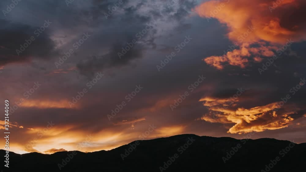 Zoom out time lapse of sun setting behind the mountains with dramatic clouds in the sky during warm summer evening Northern Norway above the Arctic Circle Zoom out time lapse of sun setting behind the mountains with dramatic clouds in the sky during warm summer evening Northern Norway above the Arctic Circle