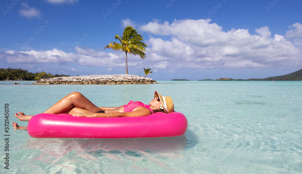 Young woman floats in paradise on a pink inflatable raft near a small tropical island on turquoise water in the South Pacific Young woman floats in paradise on a pink inflatable raft near a small tropical island on turquoise water in the South Pacific