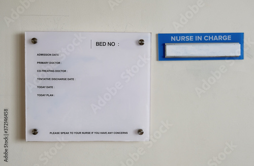 A glass information plate fixed on a hospital room wall where patient's information is written on with a name holder of the nurse on duty by the side.