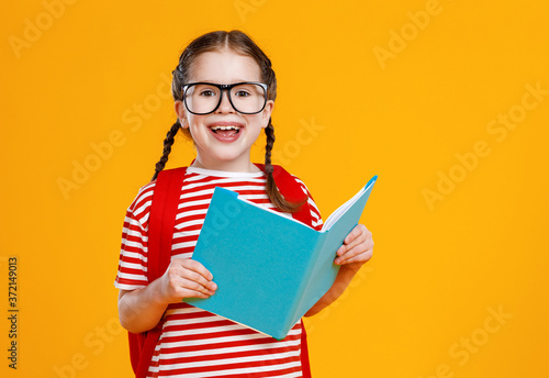 Cheerful schoolgirl smiling and reading textbook.