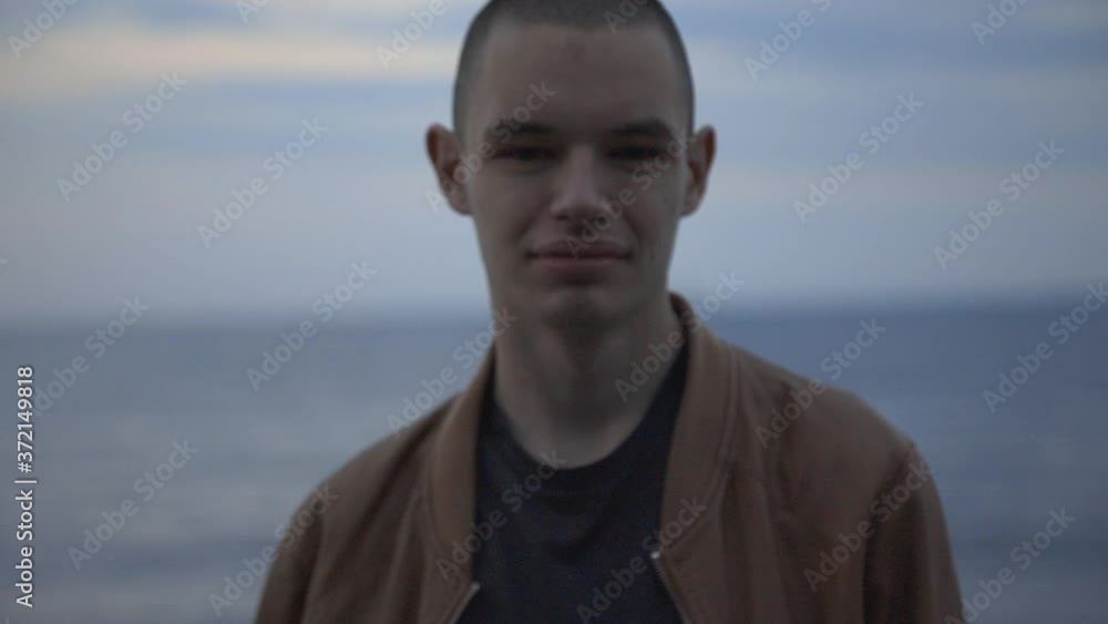 Portrait Of A Young Man Smiling Directly To The Camera With Blurry Blue Seascape Background - Closeup Shot Portrait Of A Young Man Smiling Directly To The Camera With Blurry Blue Seascape Background - Closeup Shot