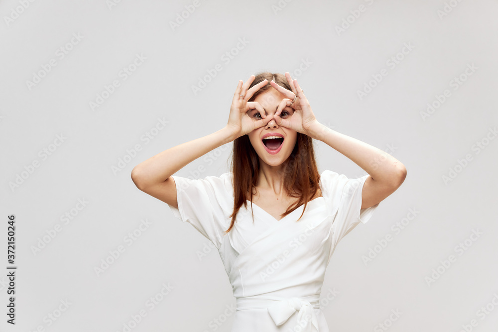 Woman holds her hands near her face in the form of a mask smile white dress 