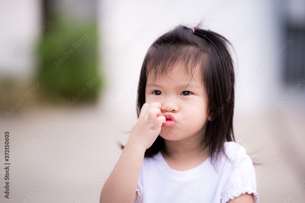 Happy girl is using her hand scratching her face and making a puckered up mouth in a good mood. Child aged 3 year old wear white shirt for walk in summer evenings or spring in front of the house. Happy girl is using her hand scratching her face and making a puckered up mouth in a good mood. Child aged 3 year old wear white shirt for walk in summer evenings or spring in front of the house.