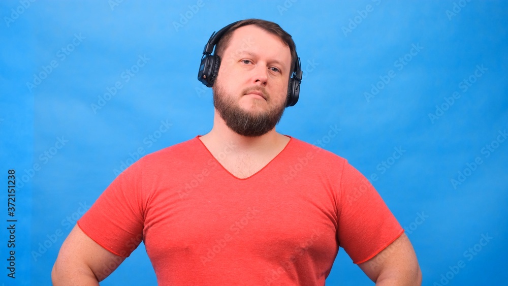Fototapeta premium Cheerful charismatic fat man in headphones isolated and pink t-shirt on a blue background. listen to music, sing and dance