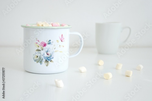 Container with marshmallows and white coffee cup on white background
