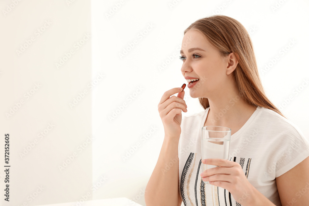 Young woman with glass of water taking vitamin capsule on light background. Space for text Young woman with glass of water taking vitamin capsule on light background. Space for text