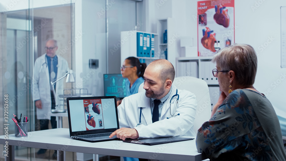 Obraz premium Doctor presenting potential heart problems to old retired elderly patient. Heart disease problems presented by cardiologist cardiology, heart attach. Health care in modern private clinic. Medical