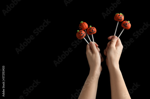 Woman with delicious pumpkin shaped cake pops and space for text on black background, closeup. Halloween celebration