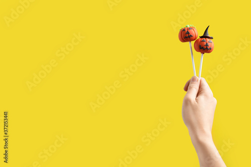 Woman with delicious pumpkin shaped cake pops and space for text on yellow background, closeup. Halloween celebration
